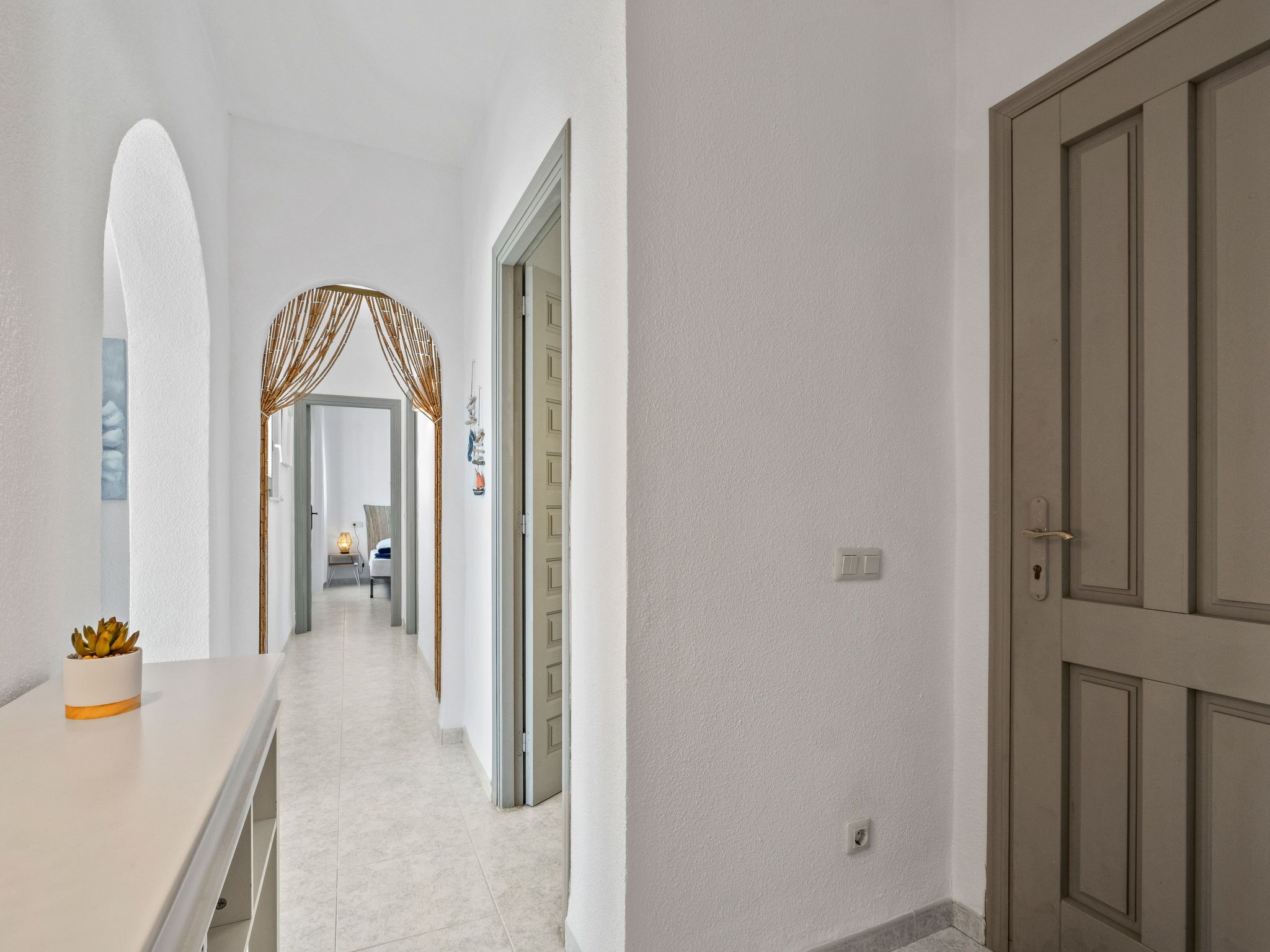 A hallway with a modern design, featuring a white wall, a wooden door, and a glass door leading to another room.