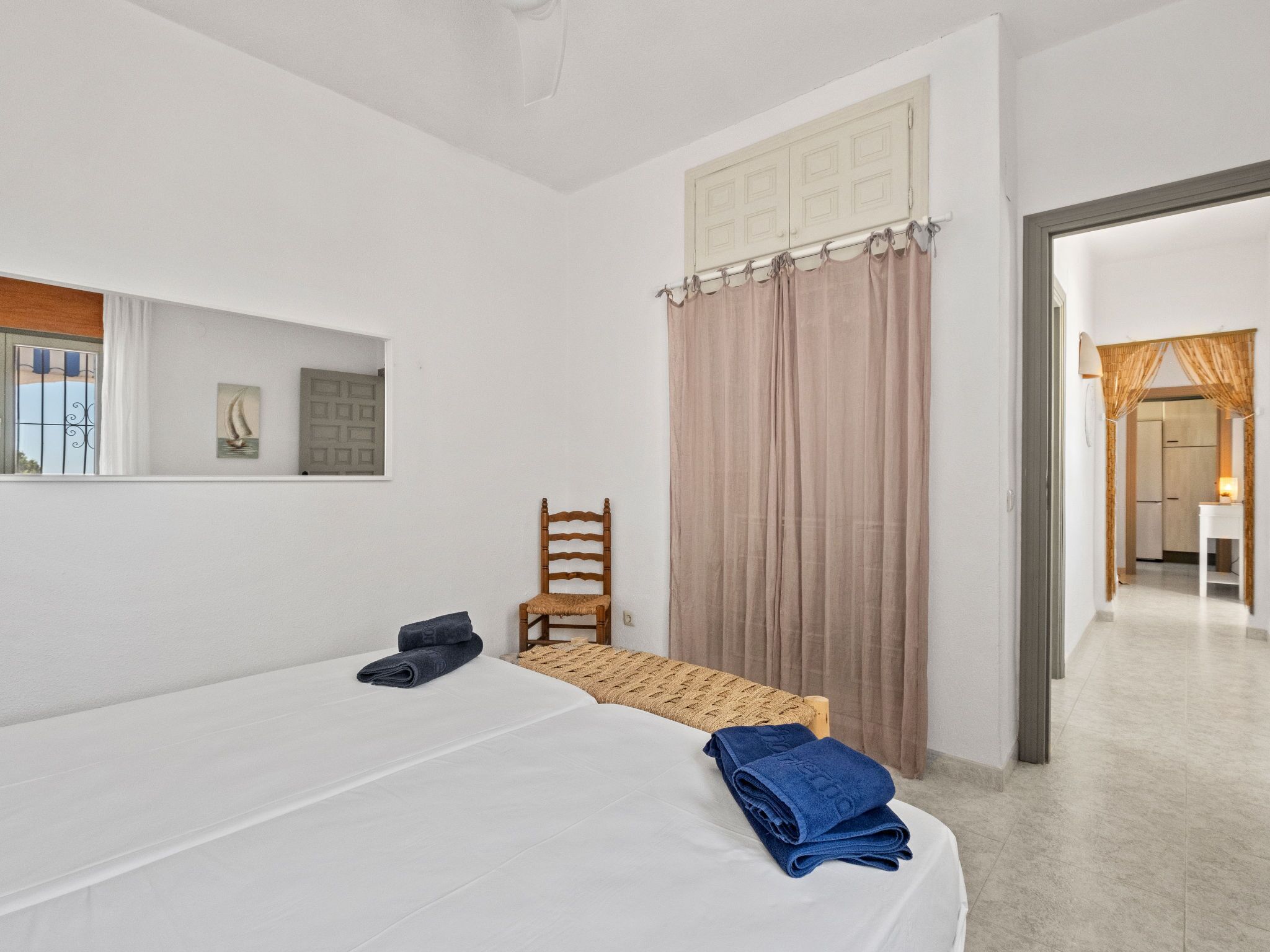 Ein Schlafzimmer mit einem Bett, einem Stuhl, einem Schreibtisch, einem Spiegel und einem Fenster mit Vorhängen.