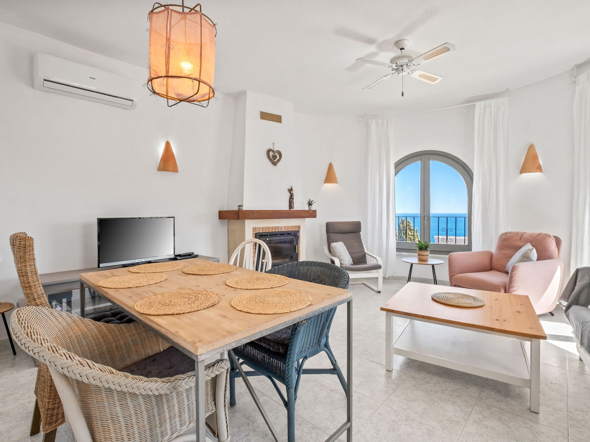 Una sala de estar moderna con comedor, chimenea, televisor y balcón con vistas al mar.