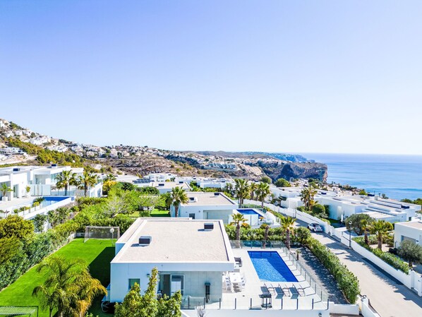 A coastal resort with modern white buildings, a swimming pool, and a view of the sea and cliffs.