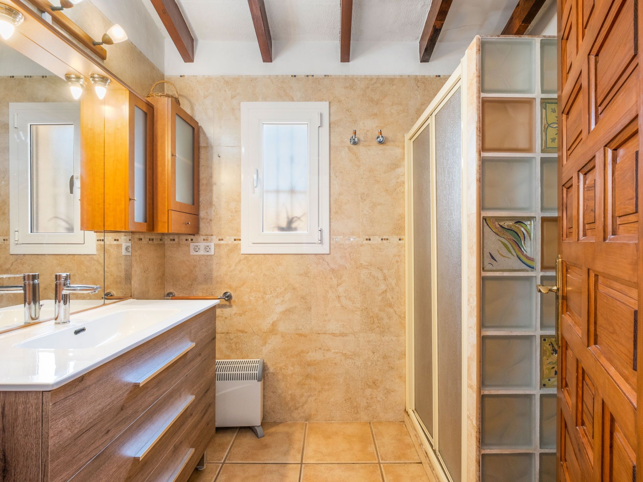 Un baño con tocador de madera, un espejo grande, cabina de ducha y suelo de baldosas.
