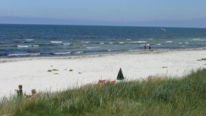 Une plage de sable blanc, quelques personnes qui se promènent et un bateau sur l’eau.