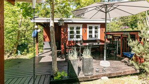 Une terrasse en bois avec une table et des chaises, un grand parasol et un bâtiment portant une pancarte indiquant « PRIVÉ ».