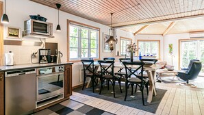 Une cuisine moderne équipée d’un four encastré, d’un four à micro-ondes et d’une machine à café. On y trouve un coin repas avec une table et des chaises en bois, ainsi qu’un canapé à l’arrière-plan.