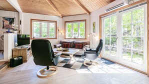 Une pièce chaleureuse avec un plafond en bois, de grandes fenêtres, un canapé, un fauteuil et un téléviseur.