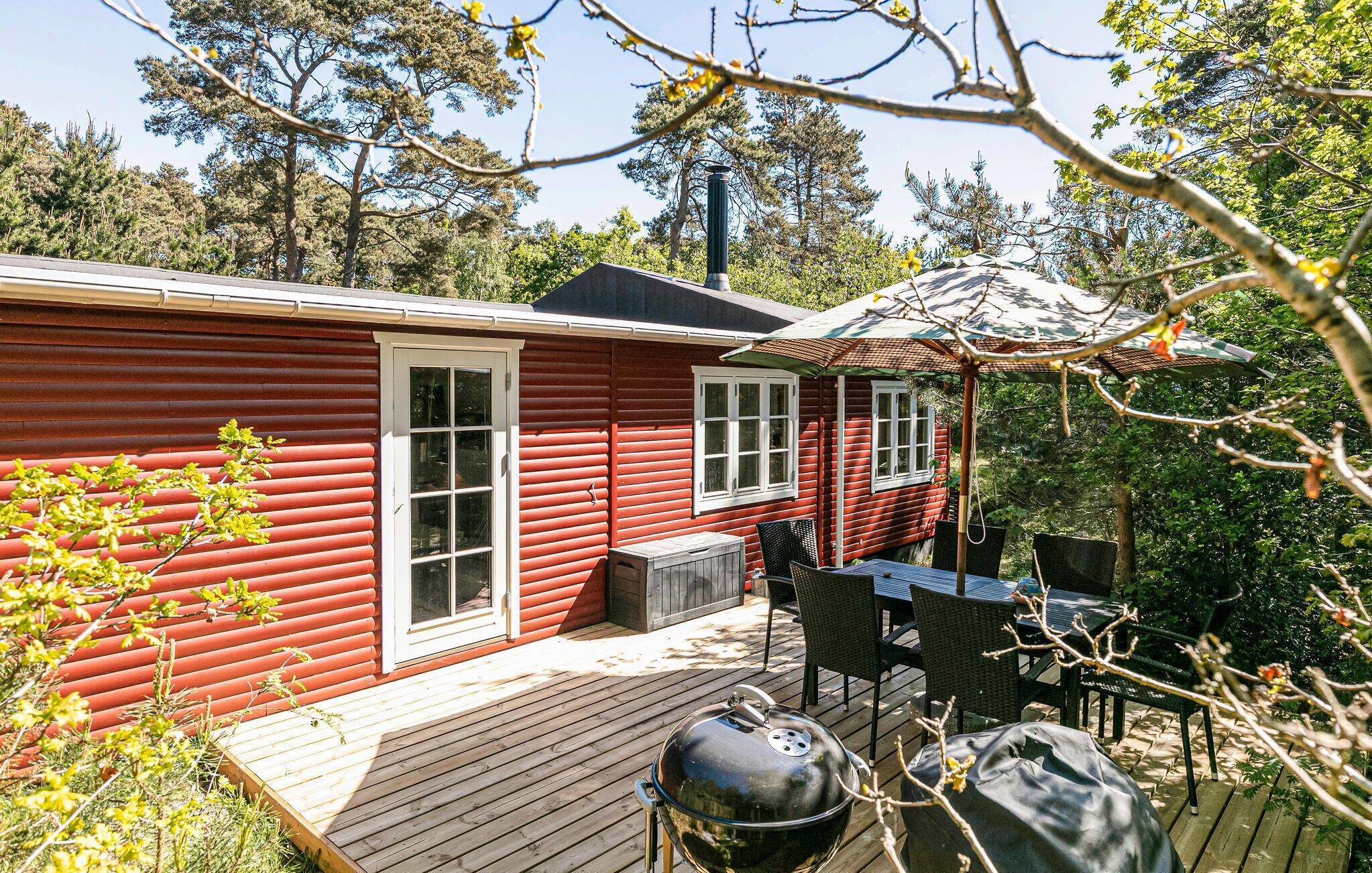 A red cabin with a deck, outdoor seating, and a barbecue grill.