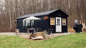 Un piccolo chalet di legno scuro, con una porta, finestre e un'area grill coperta.