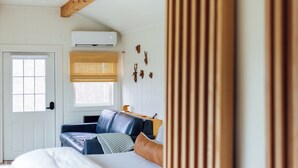 Una stanza con un letto, un divano blu, una testiera in legno, un condizionatore d'aria, una finestra con persiane e una porta.