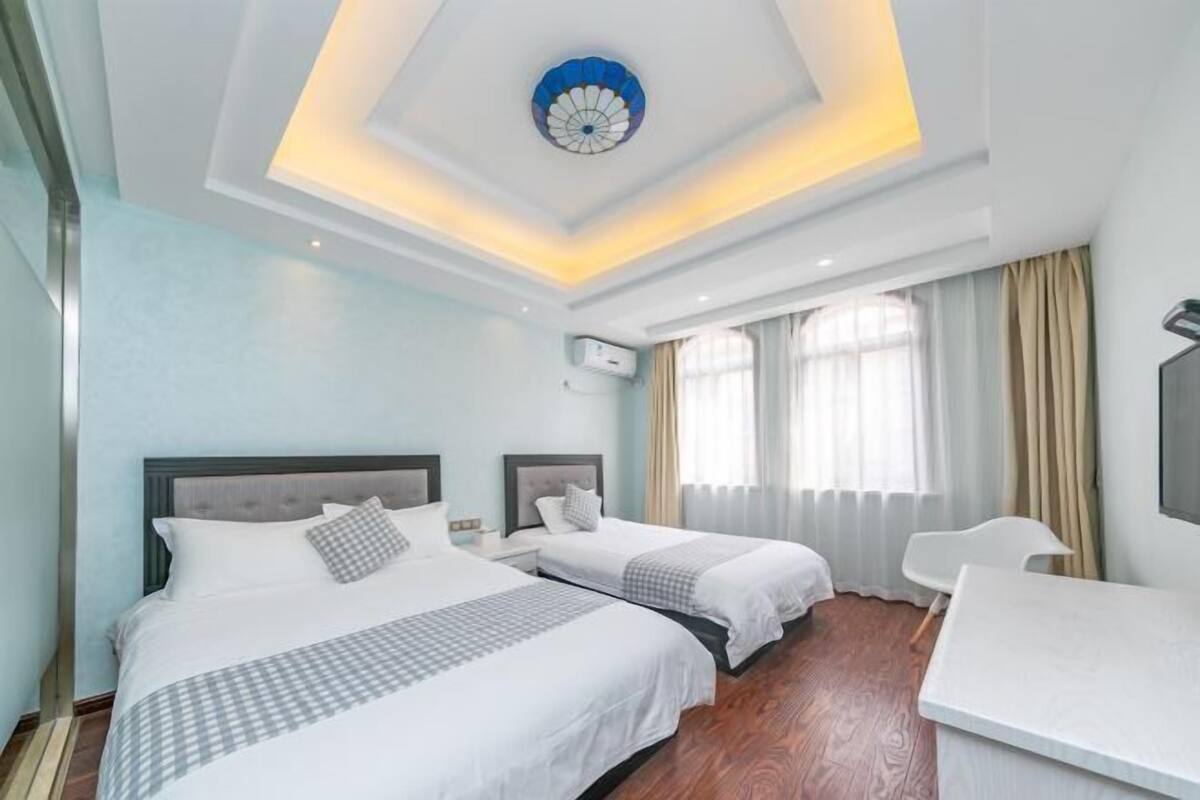A hotel room with two beds, a desk, and a ceiling light fixture.