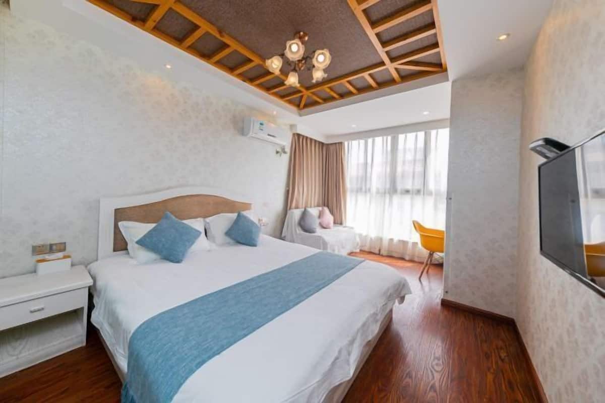A modern hotel room with a large bed, a TV, a desk, and a window with curtains.