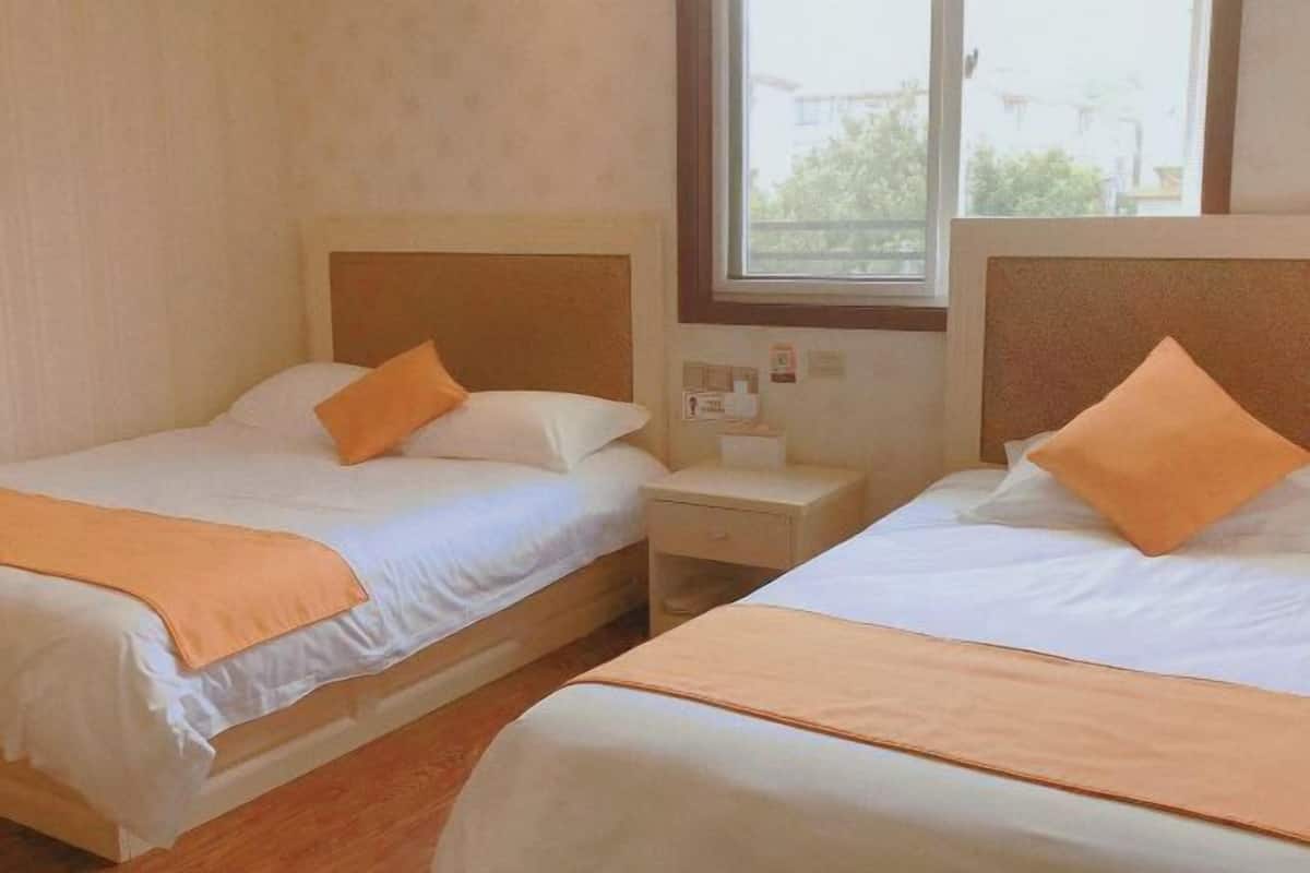 Two single beds with wooden headboards, white bedding, and orange throw pillows.