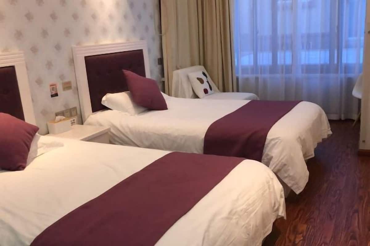 A hotel room with two beds, each with a white and maroon bedspread, a headboard, and a nightstand.