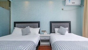 A hotel room with two beds, each with a grey checkered bedspread and white pillows. There is a small bedside table with a lamp and a tissue box. The room has light blue walls and a wooden floor. - Zhujiajian Coast Chaosu Art Inn (Zhoushan)