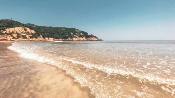 A beach with clear water, a sandy shore, and a rocky cliff with vegetation. - Zhujiajian Coast Chaosu Art Inn (Zhoushan)
