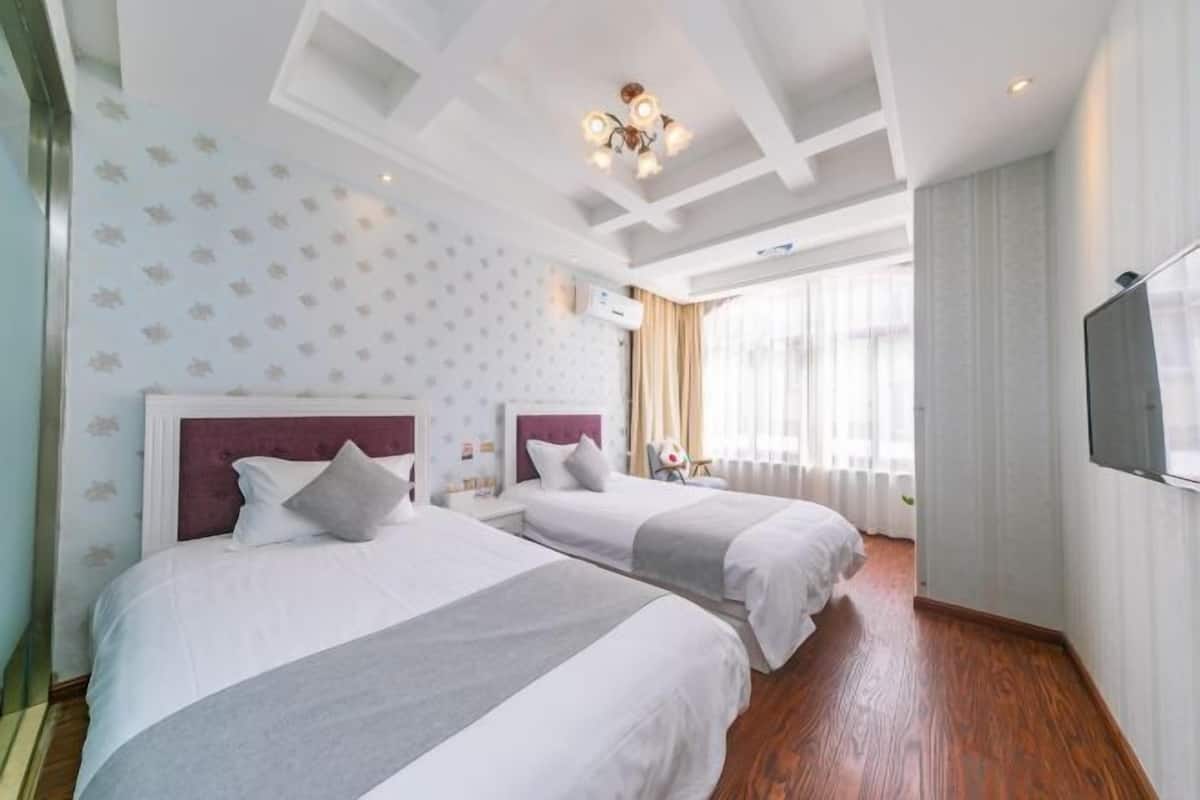 A hotel room with two beds, a TV, a chandelier, and a large window with curtains.