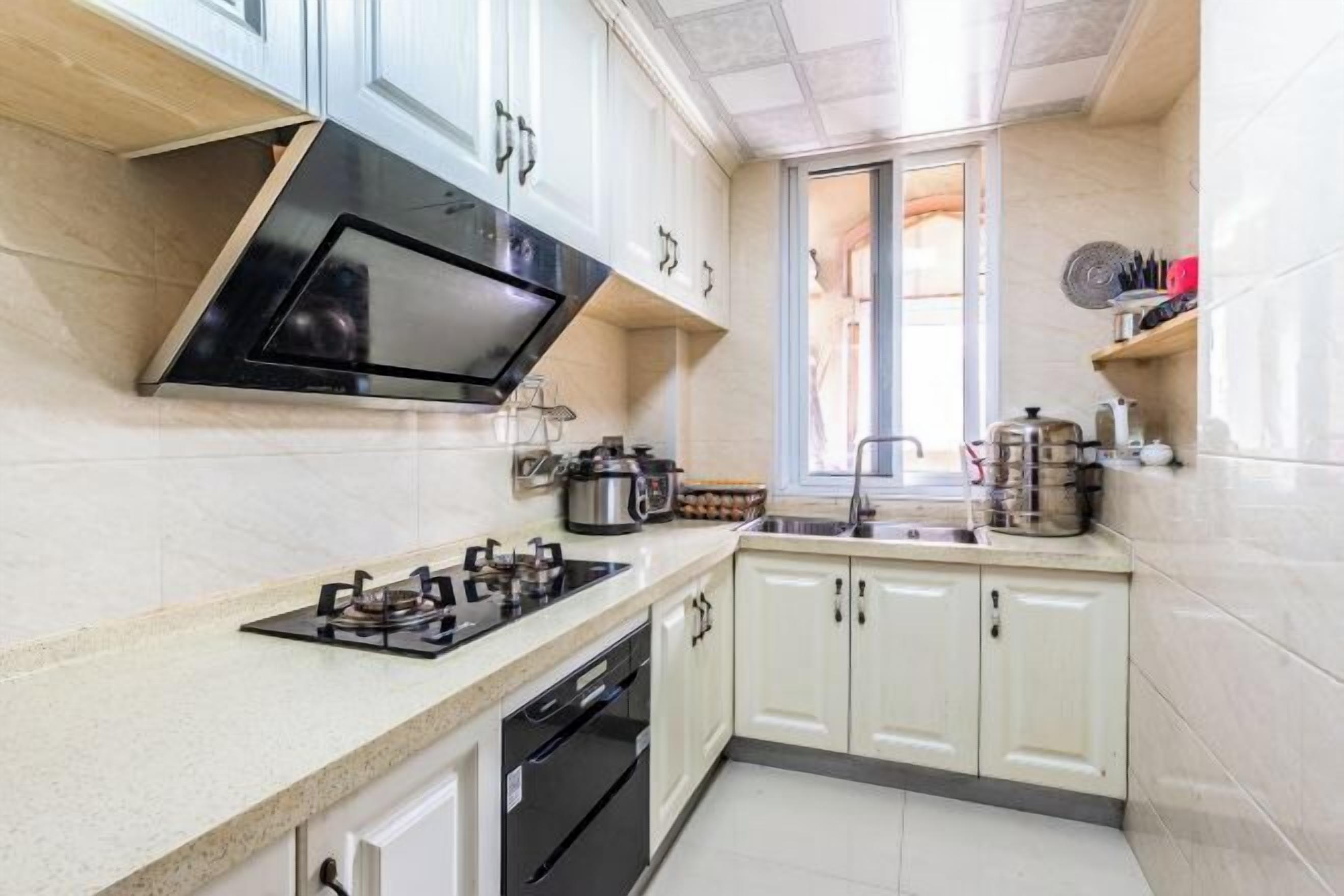 A modern kitchen with white cabinets, a black stove, and a window providing natural light.