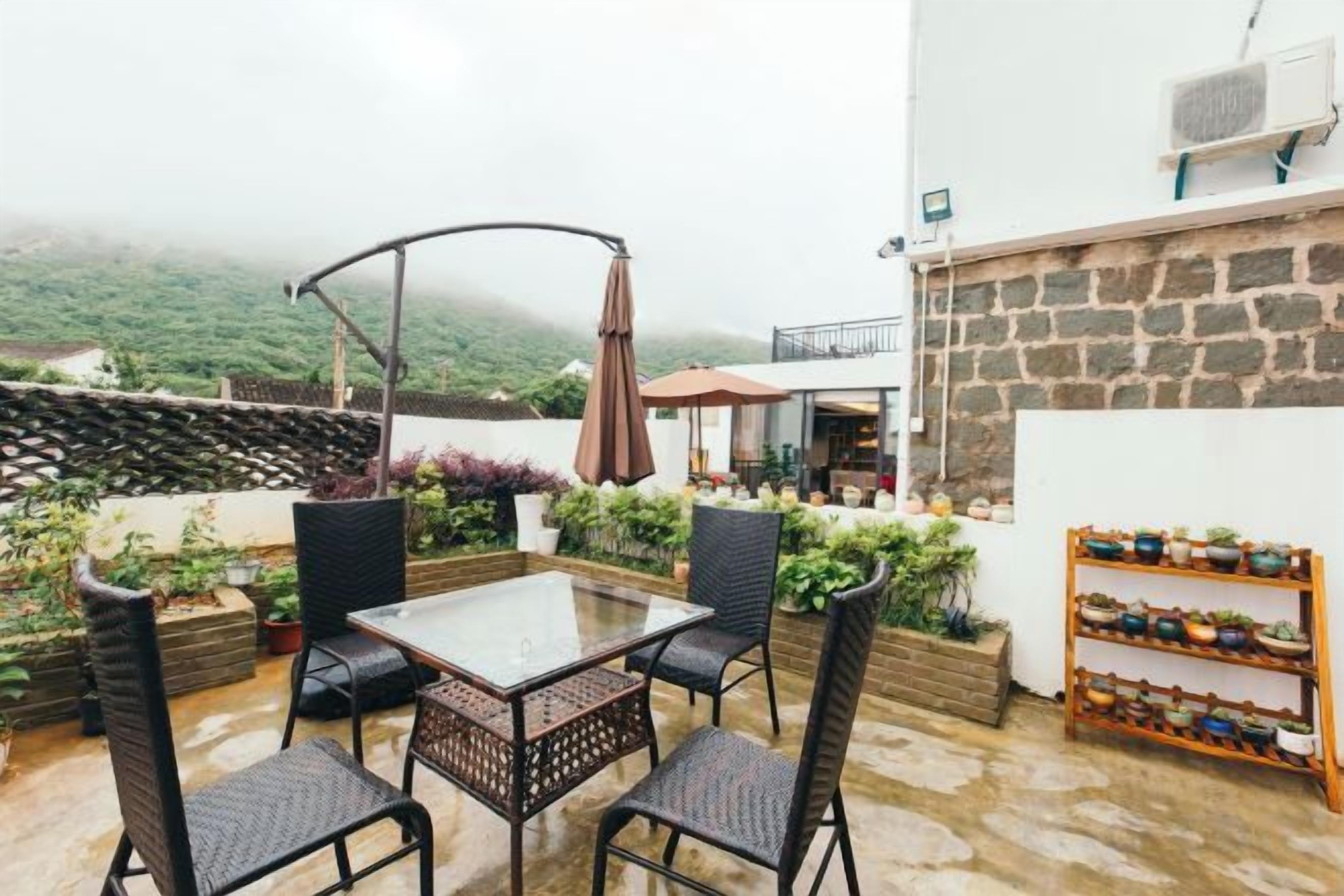 Eine Terrasse im Freien mit Tisch und Stühlen, umgeben von Pflanzen und einer Steinmauer.