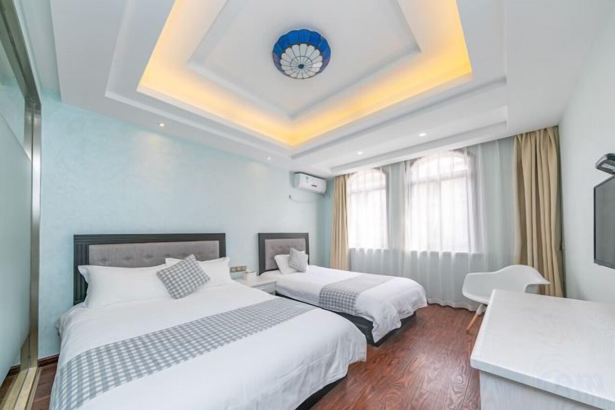 A hotel room with two beds, a desk, and a large window with curtains.