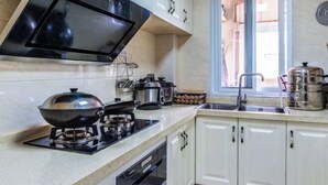 A kitchen with white cabinets, a gas stove, a microwave, and a window with a view. - Zhujiajian Coast Chaosu Art Inn (Zhoushan)