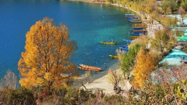 A lakeside view with boats docked along the shore, surrounded by autumn foliage. - Juxian Boutique Homestay（South Gate of Ancient City） (Lijiang)