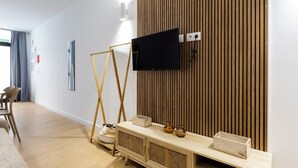 Une chambre d’hôtel moderne avec un mur recouvert de panneaux en bois, un téléviseur à écran plat fixé au mur, une console en bois agrémentée d’objets décoratifs et un chevalet.