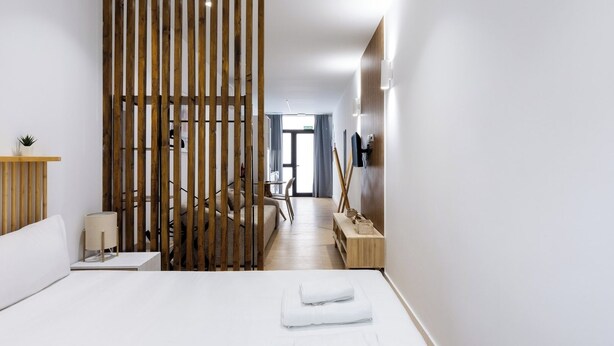 Une chambre d’hôtel moderne dotée d’un grand lit, d’une cloison en bois, d’un bureau avec une chaise et d’un téléviseur fixé au mur.