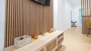 A modern living room with a wooden slat wall, a flat-screen TV mounted above a wooden console table, and a yellow chair in the background. - VLC HOST - San Jacinto A (Valencia)