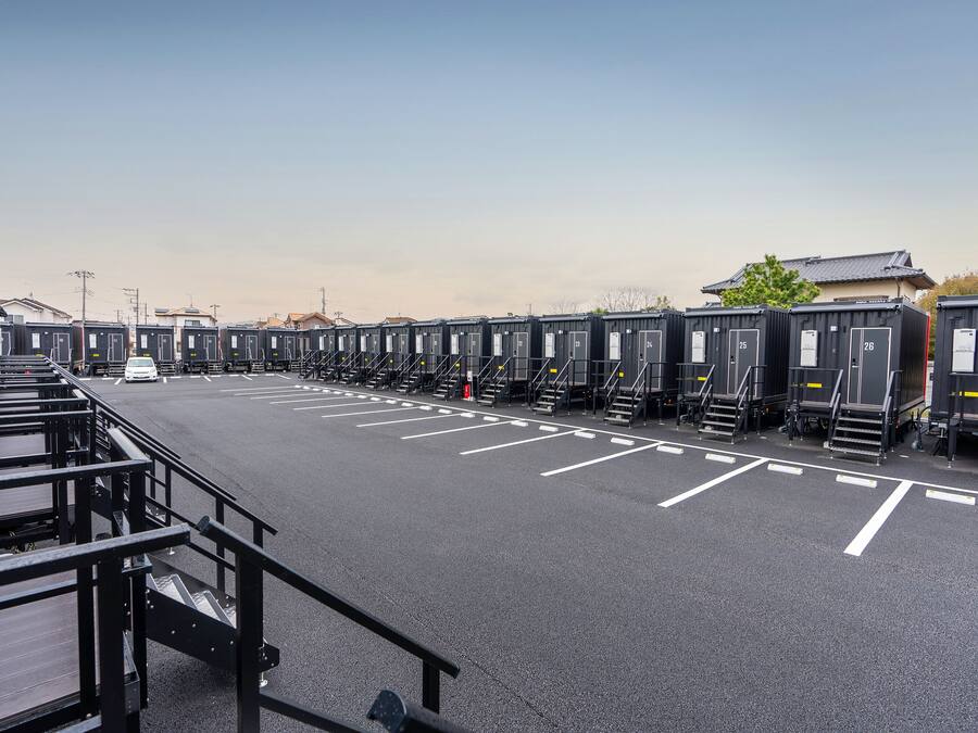 A row of portable cabins with white parking lines and a staircase leading to a building.