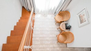A staircase with wooden steps and a white railing, leading to a landing area with two wicker chairs and a framed picture on the wall.