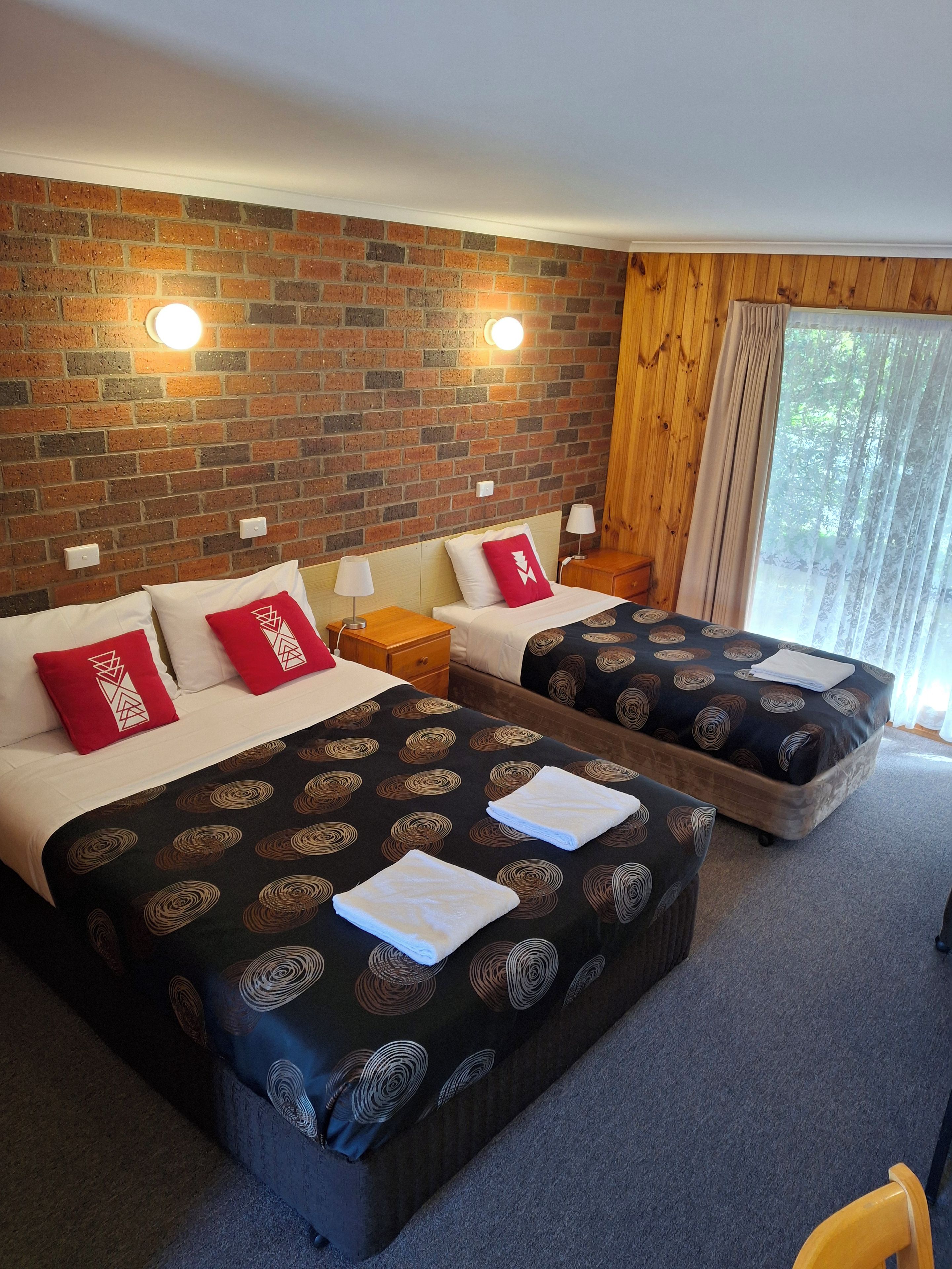 Ein Hotelzimmer mit zwei Betten, einer Ziegelwand und einem Fenster mit Vorhängen.