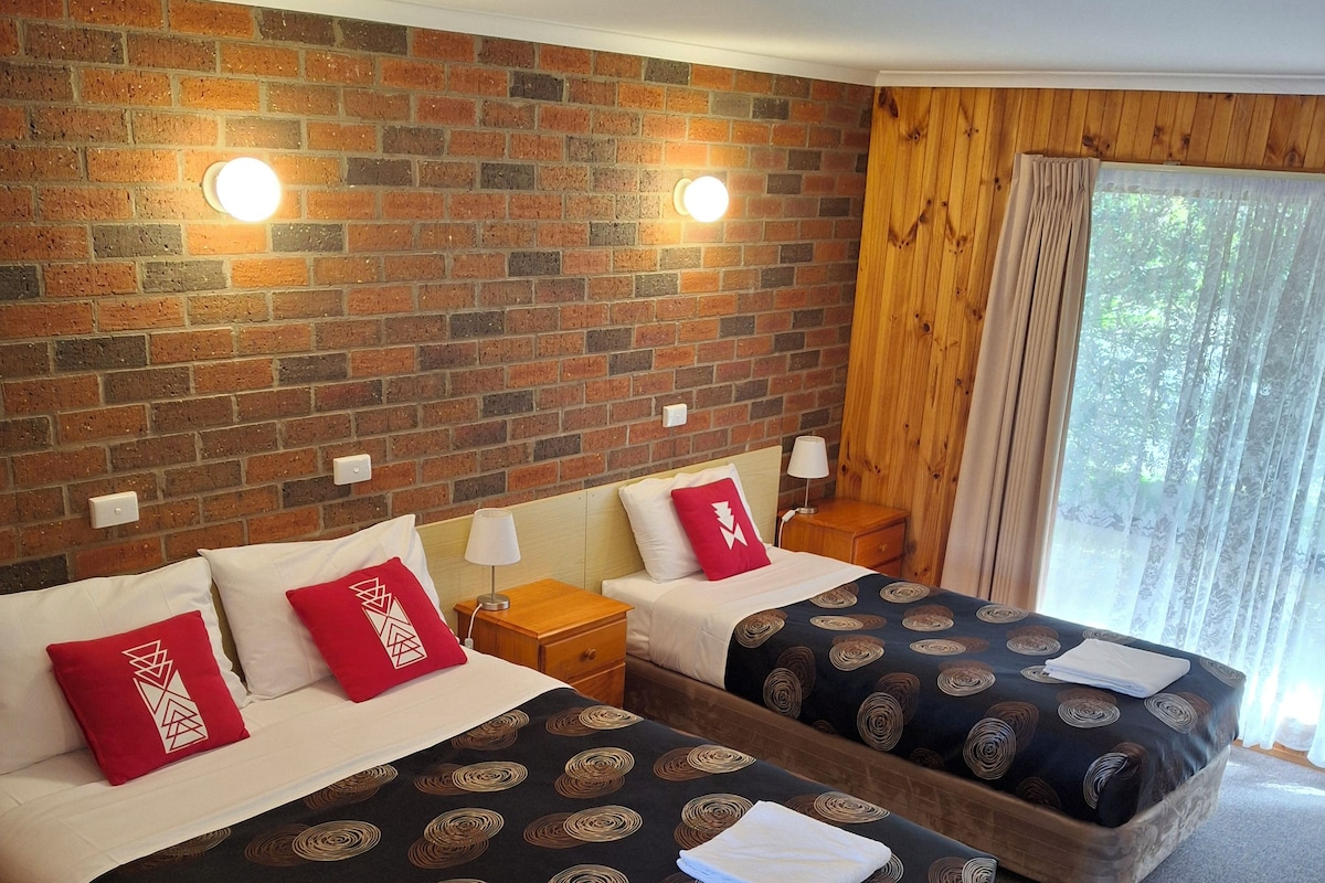 A hotel room with two beds, a brick wall, and a window with curtains.