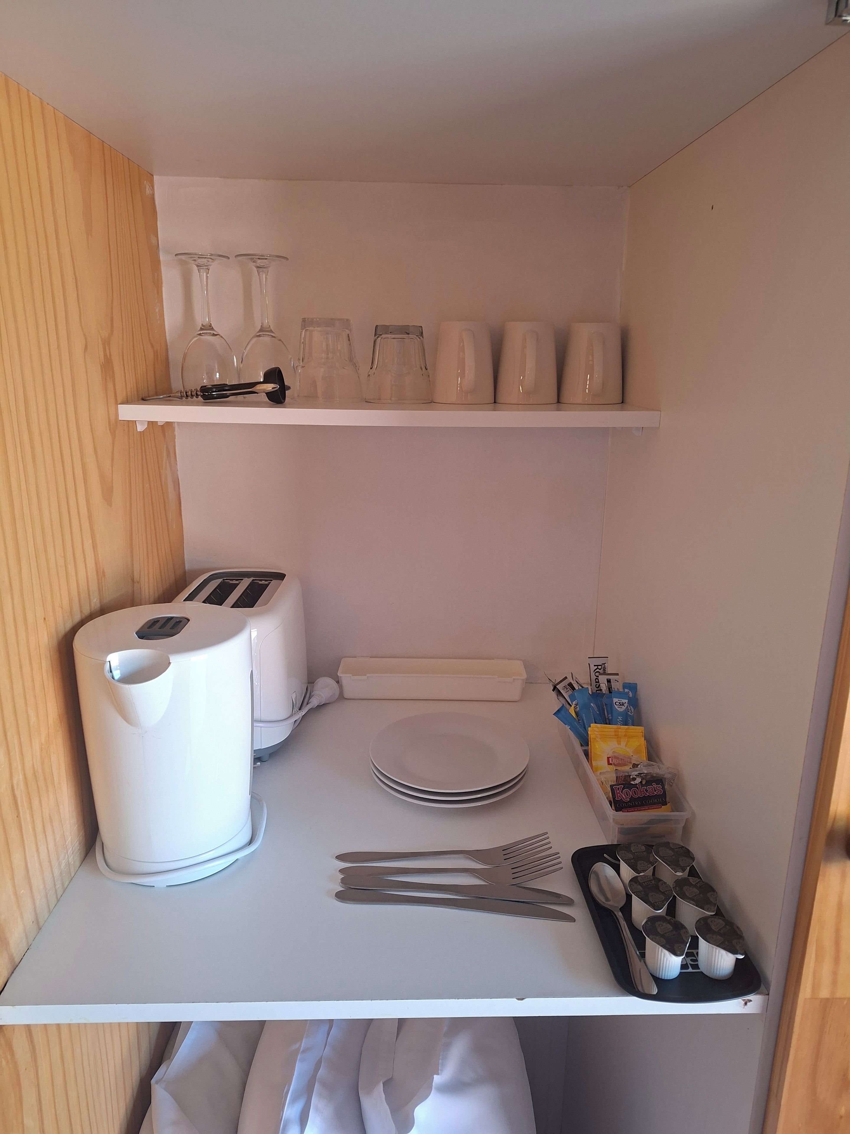 A kitchenette with a toaster, a kettle, a coffee maker, a set of plates, cutlery, and a container of Kookalats.