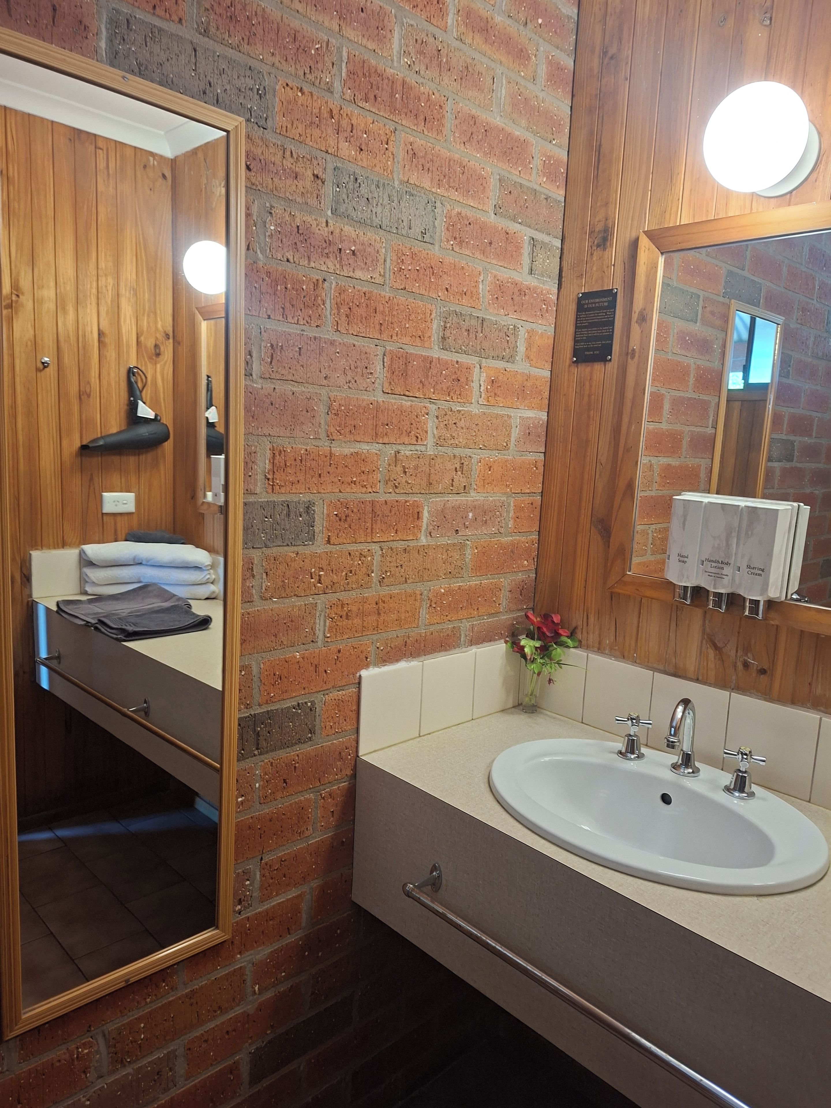A bathroom with a wooden vanity, a large mirror, a sink with two faucets, and a towel rack.