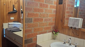 A bathroom with a wooden vanity, a large mirror, a sink with two faucets, and a towel rack.