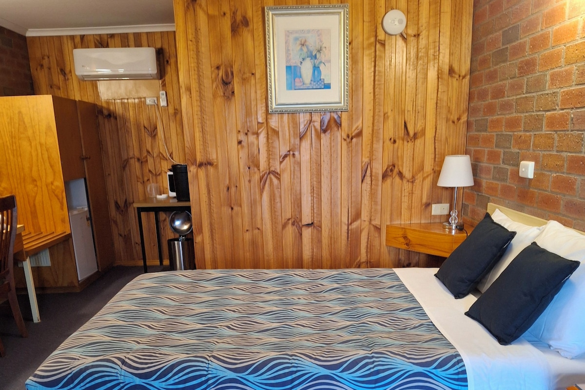 A room with a bed, a desk, a chair, a lamp, and a picture on the wall.
