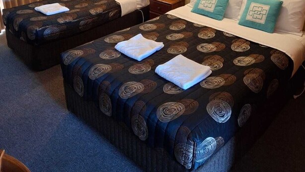 Quarto de hotel com duas camas, parede de tijolos e painel de madeira à esquerda.
