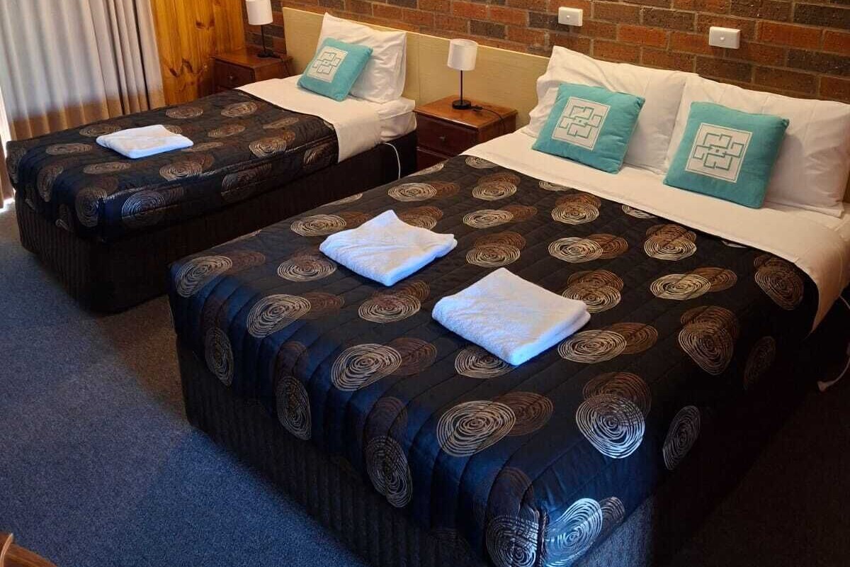 A hotel room with two beds, a brick wall, and a wooden panel on the left.
