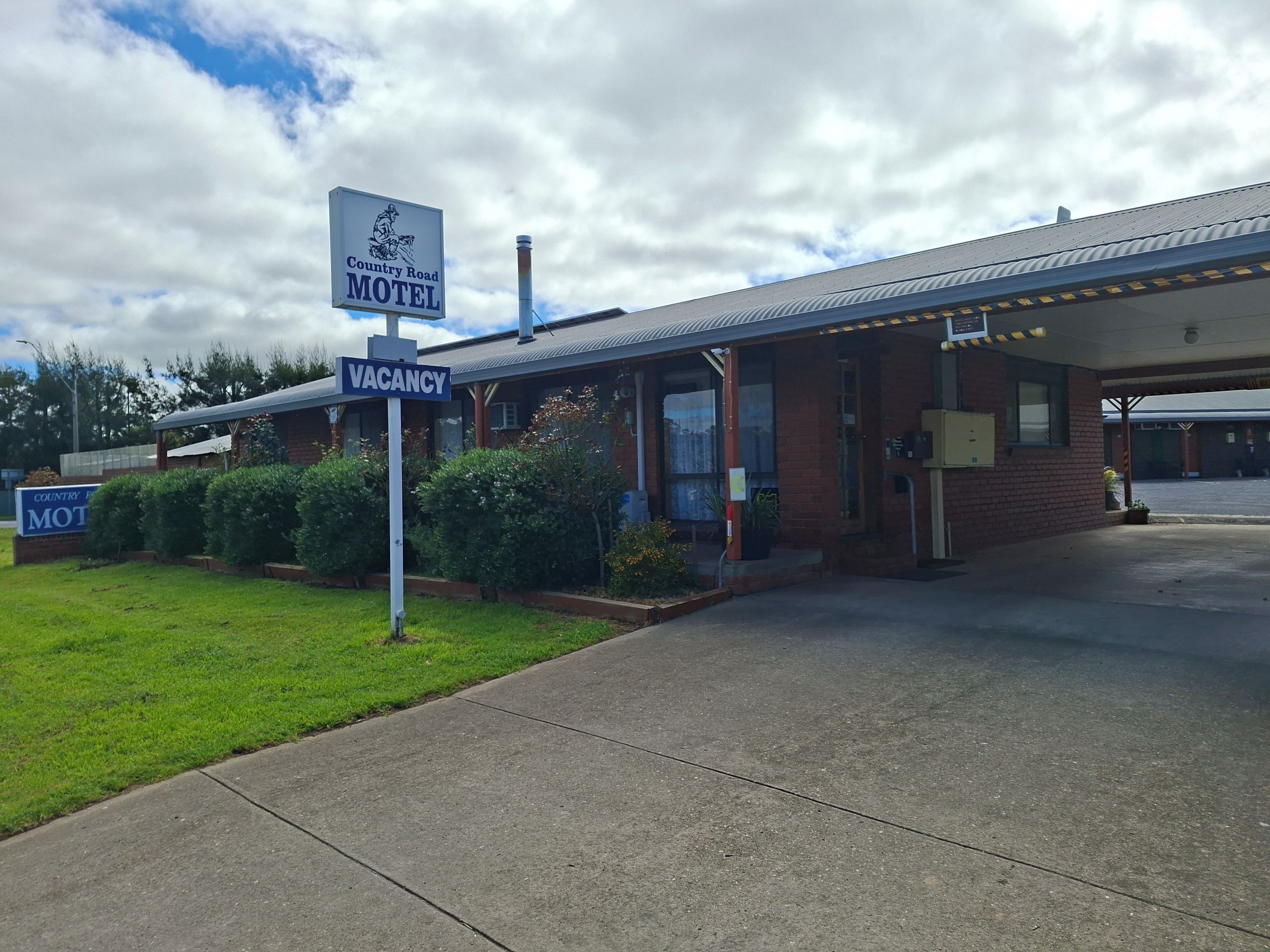 A motel with a 'VACANCY' sign, a covered parking area, and a brick building.