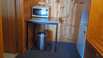 Una stanza compatta con parete in legno, un piccolo tavolo con forno a microonde, cestino e frigorifero.