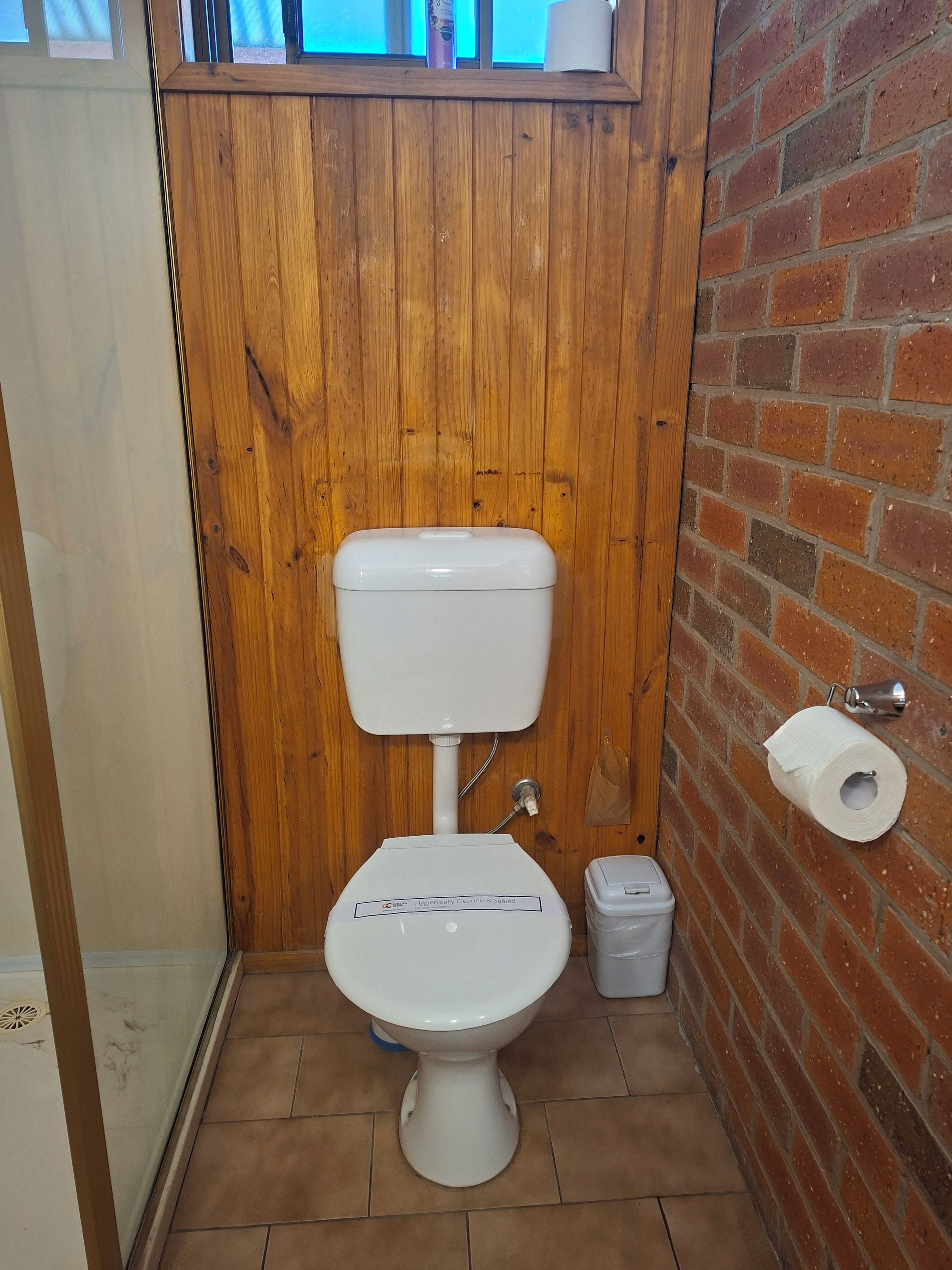 A small, compact bathroom with a white toilet, a trash bin, and a toilet paper holder on the wall.