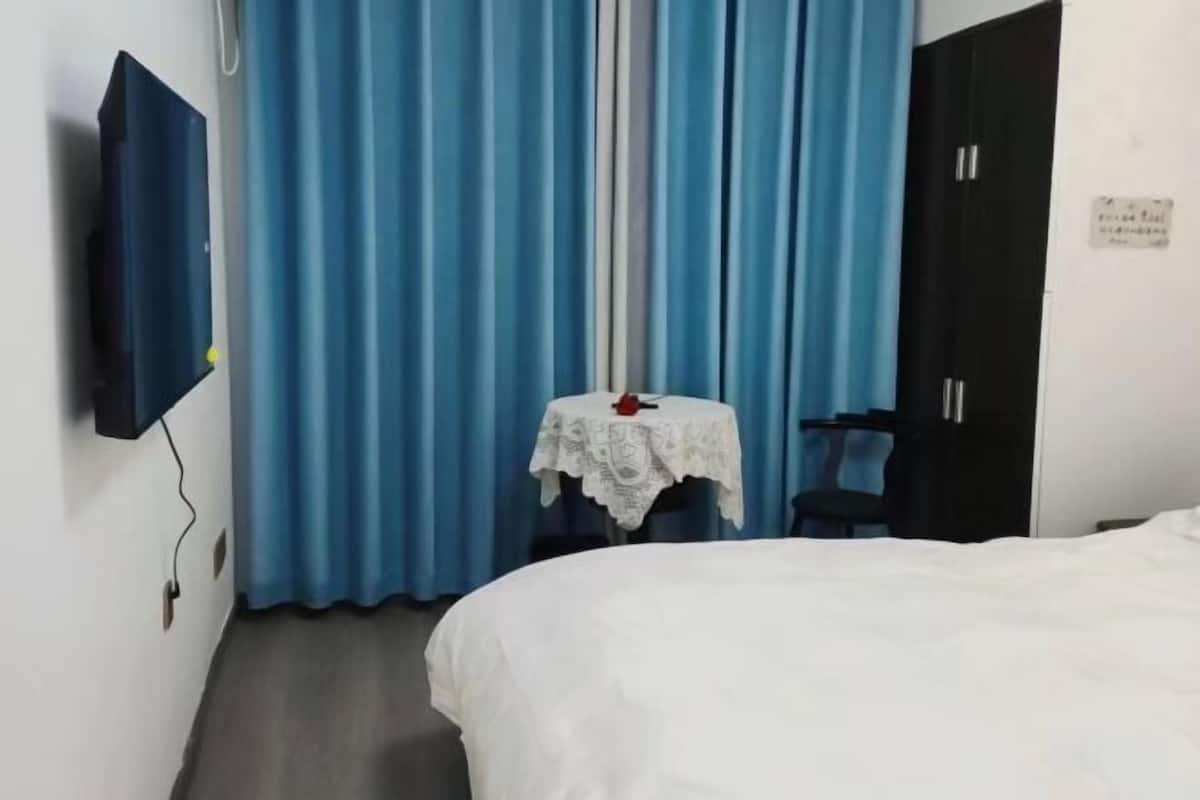 Habitación de hotel con cama, una mesita con mantel de encaje, una silla, televisor montado en la pared y un armario.