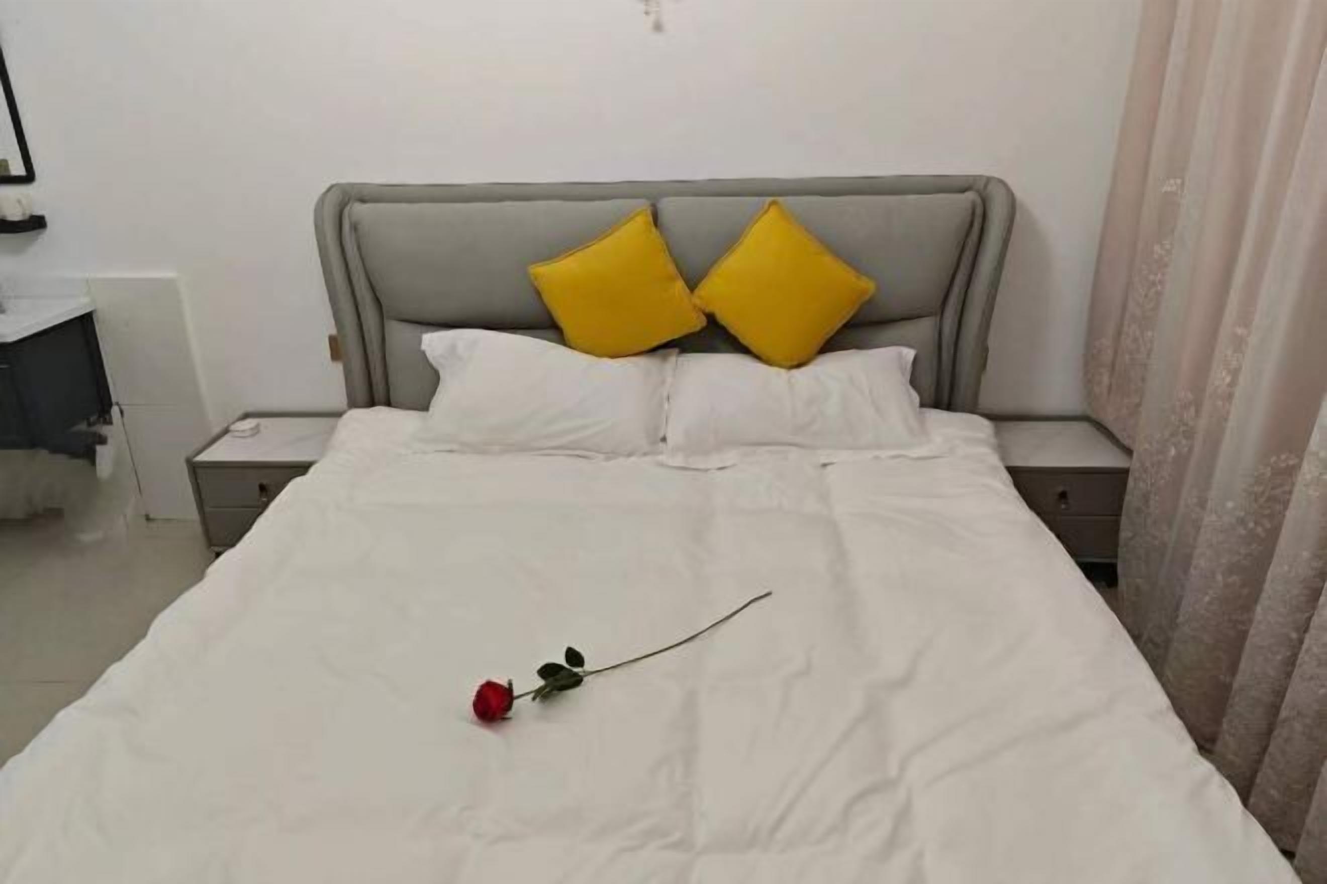 A neatly made bed with white bedding, two pillows, and a single red rose.