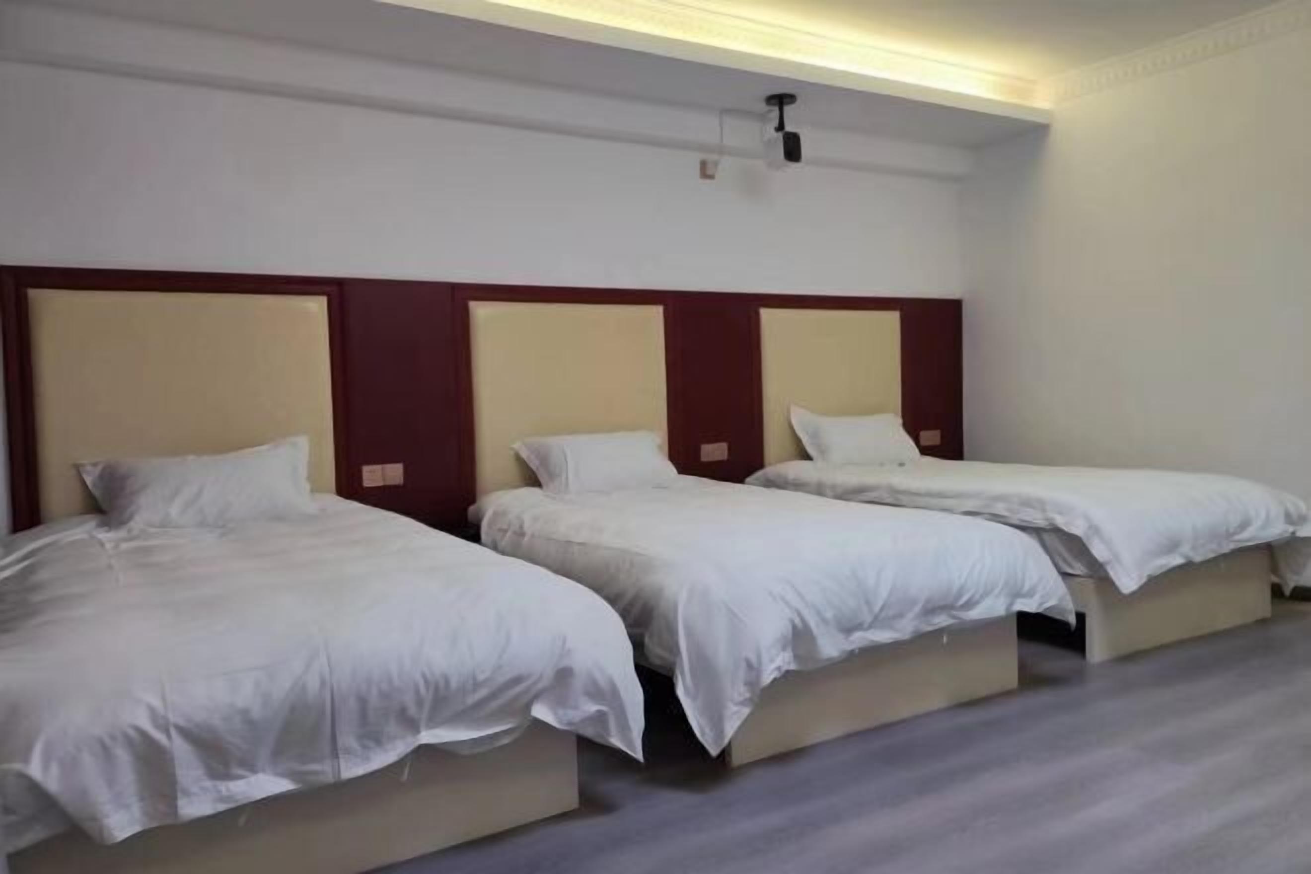 A hotel room with three single beds, a wooden headboard, and a ceiling light fixture.