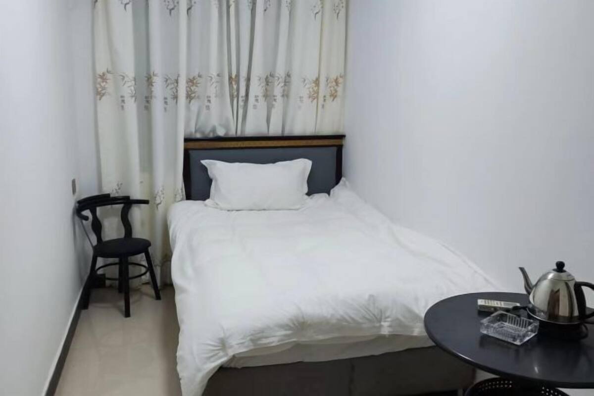 Una habitación de hotel pequeña con una cama individual, una silla, una mesa con un hervidor y una cortina con estampado floral.