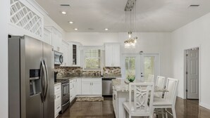 Una cocina moderna con armarios blancos, electrodomésticos de acero inoxidable y un comedor con sillas blancas y encimera de mármol.