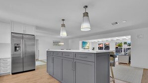 Una cucina moderna con mobili grigi, un frigorifero in acciaio inossidabile e illuminazione a sospensione.