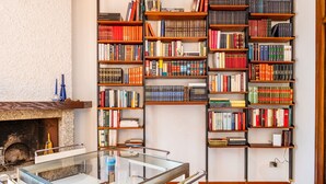 Eine Bibliothek mit mehreren Bücherregalen voller Bücher, einem Glastisch mit Metallstühlen und einem Kamin.