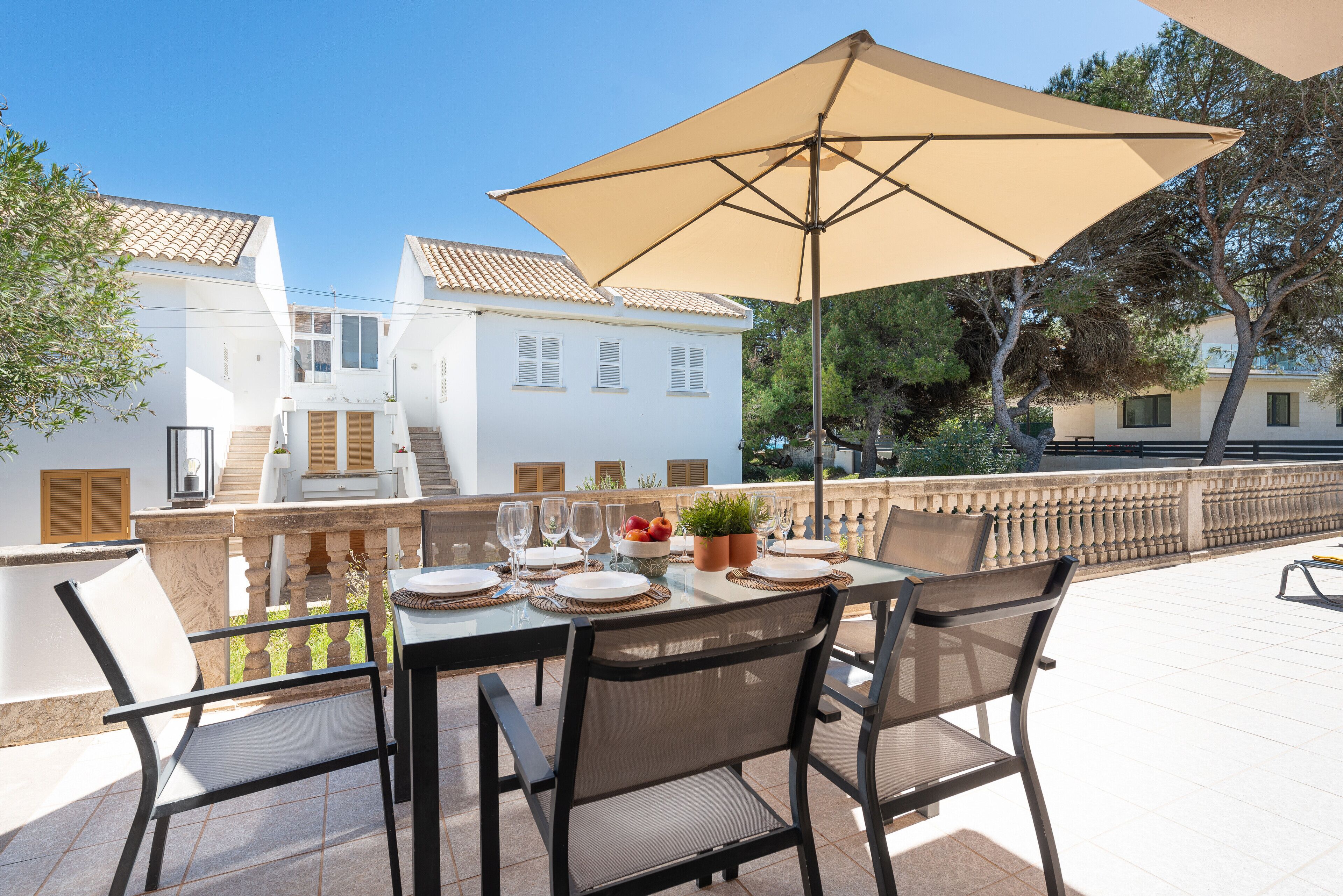 An outdoor dining area with a table set for four, surrounded by chairs, under a large umbrella.