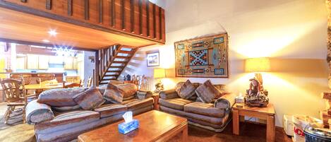 Una sala de estar acogedora con una escalera de madera, un gran tapiz en la pared y un comedor al fondo.