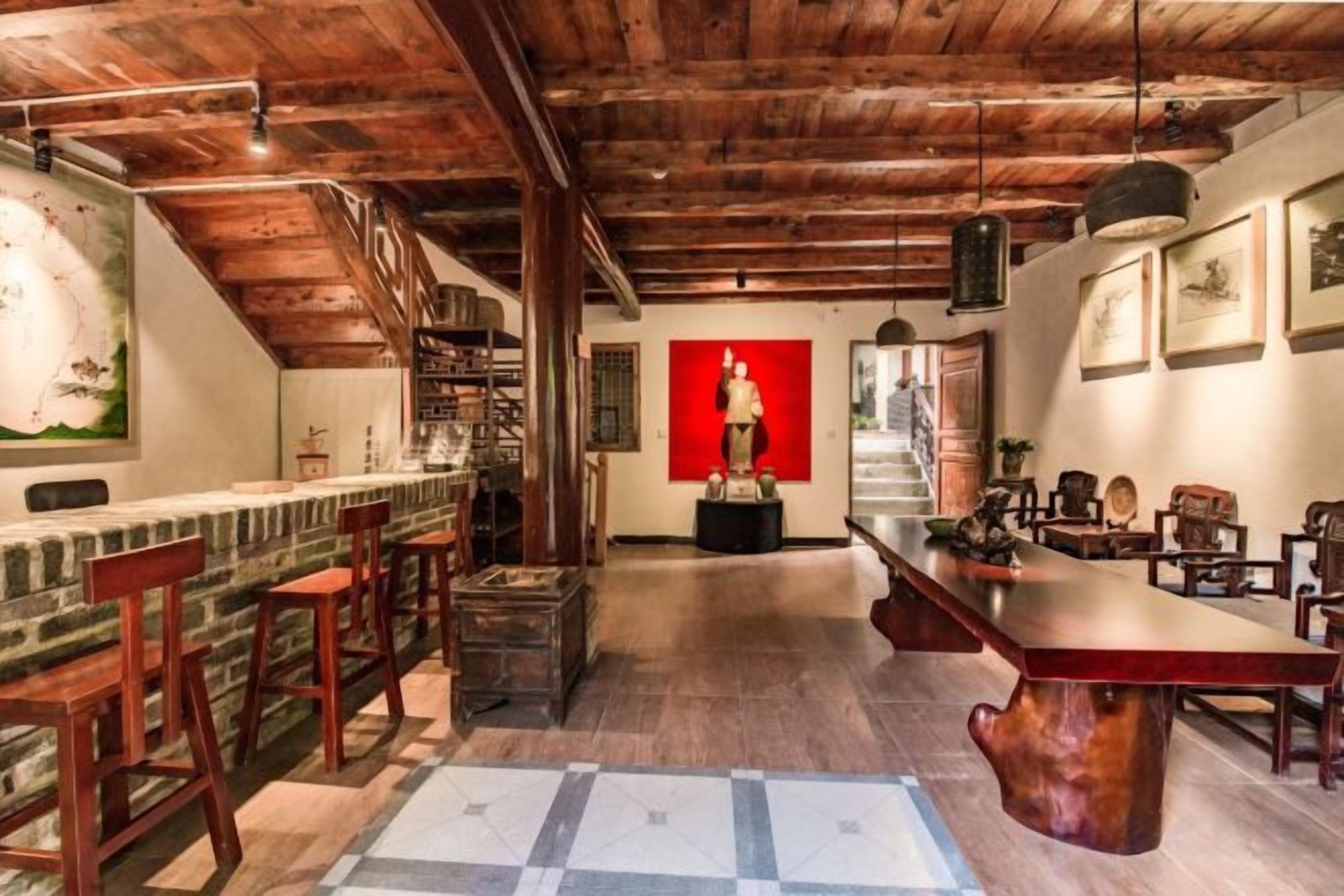 A spacious room with a long wooden bar, multiple seating areas, and a view of a red statue in the background.